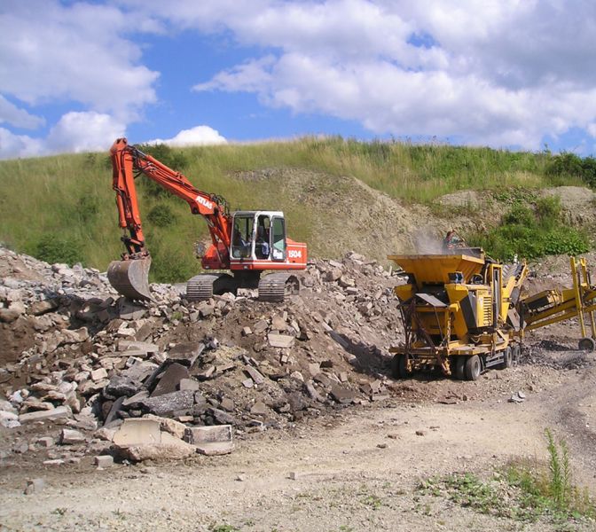 Bagger und Förderungsmaschine bearbeiten einen Schuttberg